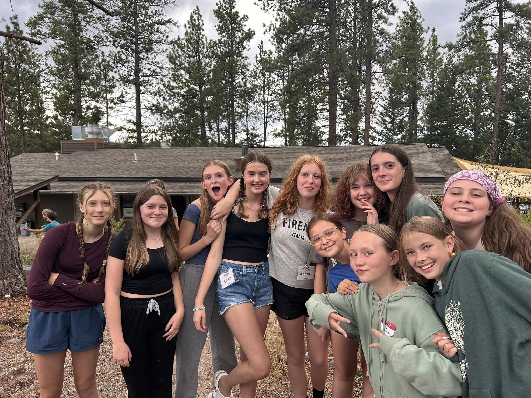 Group of young performers posing for a photo at a camp. Trees and a lodge in the background.